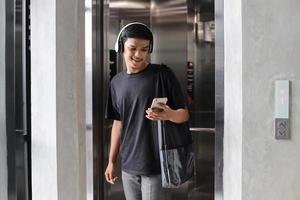 estudiante universitario asiático enviando mensajes de texto a su teléfono mientras sale del ascensor foto