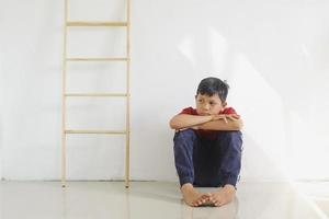 niño triste y solitario sentado solo en el suelo contra la pared foto