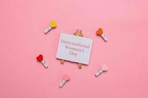 Flat lay of international women's day writing on signboard surrounded by mini hearts on clothespins on pink background photo