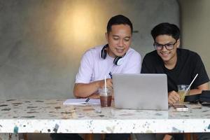 dos estudiantes universitarios asiáticos que estudian juntos usando computadoras portátiles en un café foto