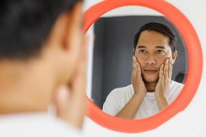 Handsome asian man looking to the mirror after shaving his beard photo
