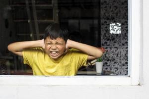 niño asiático cerrando los oídos con las manos en una posición protectora. experiencia traumática infantil, psicología psicológica, síndrome de asperger, trastorno de asperger, autista, autismo. foto