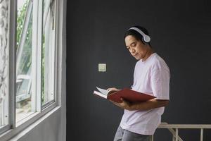 Young Asian man listening to music with headphone and reading a book at home photo