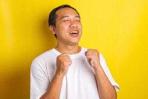 primer plano de un hombre asiático muy feliz y emocionado haciendo el gesto de ganador con una sonrisa y gritando por el logro foto