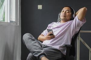 Young asian man sitting relaxing while enjoying music via mobile phone at home photo