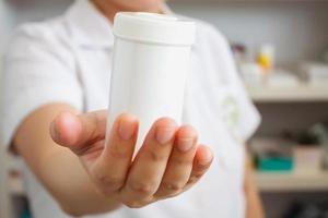 Pharmacist showing medicine bottle on her hand in the pharmacy photo