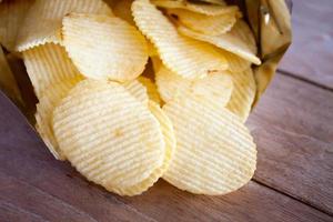 Opened pack with potato chips over wooden table photo