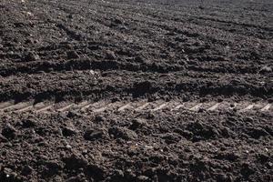 Cultivated plowed soil with rows and tractor footprint. Agricultural background texture photo