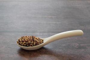 Quinoa seeds in the white spoon isolated on wooden table background.  Quinoa is a good source of protein for people following a plant-based diet.