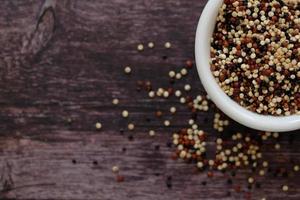 Quinoa seeds in the white cup on wooden background.  Quinoa is a good source of protein for people following a plant-based diet. photo