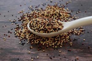 semillas de quinua en la cuchara blanca sobre fondo de mesa de madera. la quinua es una buena fuente de proteínas para las personas que siguen una dieta basada en plantas. foto
