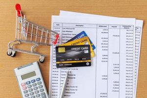 tarjetas de crédito y carrito de supermercado y calculadora en extracto bancario en una mesa de madera foto