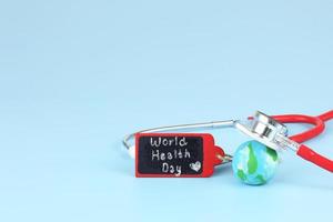 Checking health with stethoscope on world health day - blue earth with red label with text photo