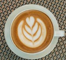 Latte art coffee cup on glass table. Blurred leaf reflection background. photo