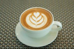 Latte art coffee cup on glass table. Blurred leaf reflection background. photo