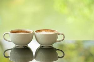 Latte art coffee cup on glass table. Blurred leaf reflection background. photo