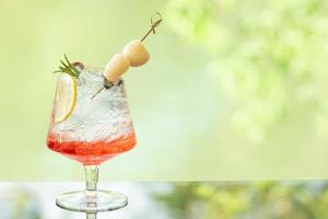 delicioso jugoso refresco de limón fresco y agua roja y lichi en la mesa de vidrio fondo de reflejo de hoja borrosa. foto