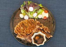 Roasted steak pork, grilled pork chops with vegetable salad and toast bread with steak sauce in black plate on the dining table food photo