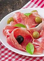 Ham, olives, basil on old wooden background photo