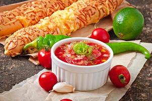 Salsa dip in bowl of bread and cheese sticks on wooden background photo