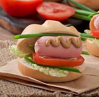 Little cheerful hot dog with sausage and tomato photo