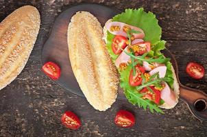 Sandwich con salchichas, lechuga, tomate y rúcula en el fondo de madera vieja foto