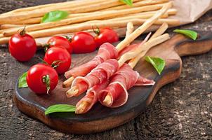 Grissini bread sticks with ham, olives, basil on old wooden background photo