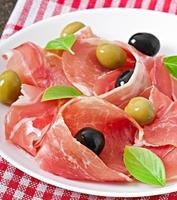 Ham, olives, basil on old wooden background photo