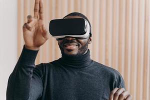 Excited African American man in VR headset glasses enjoying augmented reality in office