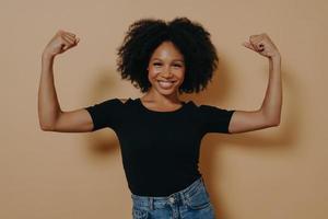 Young confident african lady in casual clothes showing strength of her arms by lifting them up