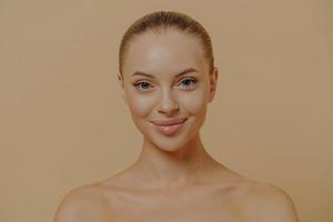 retrato de belleza de una mujer encantadora con una piel brillante y saludable posando semidesnuda contra una pared beige foto