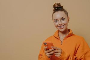 Happy attractive woman holding smartphone, ordering food online while standing isolated on beige photo