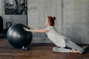 Young cheerful athletic woman with red hair exercising indoors with fitball photo