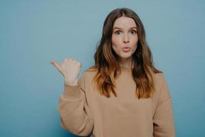 Surprised young woman pointing at copy space with wow expression photo