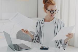 mujer joven positiva con cabello rojo calcula los cargos de servicios públicos involucrados en la planificación del presupuesto mensual foto