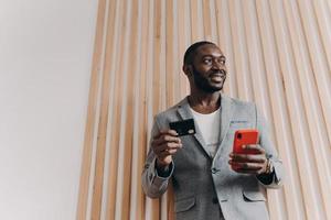 Excited African-American businessman using smartphone and credit card for shopping online photo