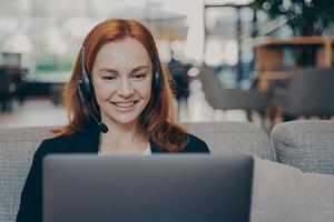 Close-up portrait of redhead entrepreneur girl, working remotely with laptop and earphones headset photo