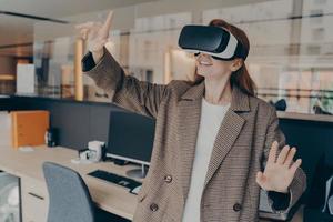 Happy female office worker in VR headset enjoying virtual reality game on her break