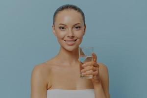 Water balance. Young healthy woman with clean skin holding glass of pure water, isolated on blue