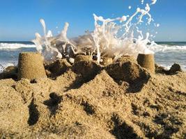 castillo de arena golpeado por una ola del mar foto