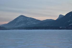 Pink Sunrise over a snowy mountain peak with frozen lake in the foreground photo