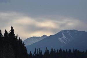 la luz del sol está bloqueada por las nubes sobre los picos de las montañas nevadas foto