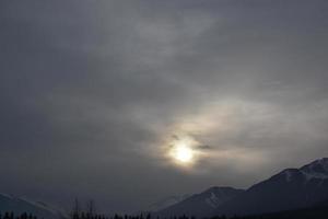 Sunlight being blocked by clouds over snowy mountain peaks photo