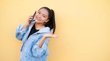 Portrait beautiful young girl wear jacket jean talking with mobile on orange bcakground,Asian girl. photo