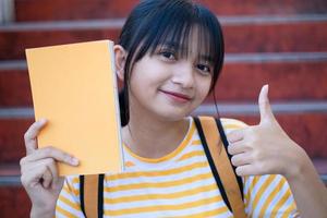 Student young girl hold yellow book sitting on stairs at school. photo