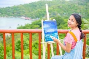 niña usando un dibujo de pincel sobre papel de lienzo, en una hermosa vista del paisaje en koh tao, tailandia. foto