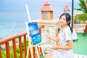 Young girl using brush drawing picture on canvas paper, at beautiful landscape view at koh tao Thailand. photo