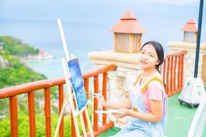 niña usando un dibujo de pincel sobre papel de lienzo, en una hermosa vista del paisaje en koh tao, tailandia. foto