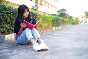 Student young girl with pink backpack sitting at on foor with school background. photo