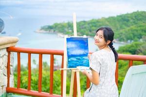 niña usando un dibujo de pincel sobre papel de lienzo, en una hermosa vista del paisaje en koh tao, tailandia. foto